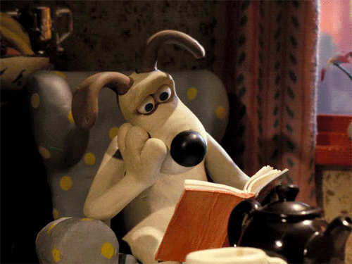 3D animated dog sitting up in an upholstered chair, holding a book in one paw and resting his head on his other paw, elbow on chair's arm. He blinks at pages in front of him.