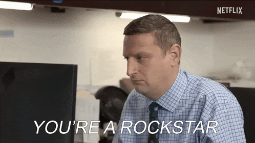 a man in a plaid shirt and tie is sitting at a desk in front of a computer and talking .