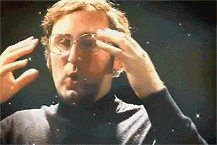 GIF of a white man in retro glasses and turtleneck making motions as if his head is exploding, as fireworks are overlayed.