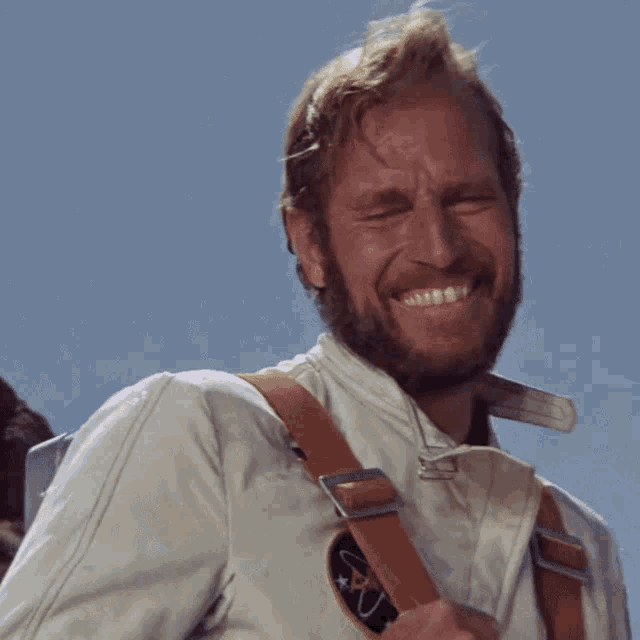 a man with a beard wears a white jacket with a nasa patch