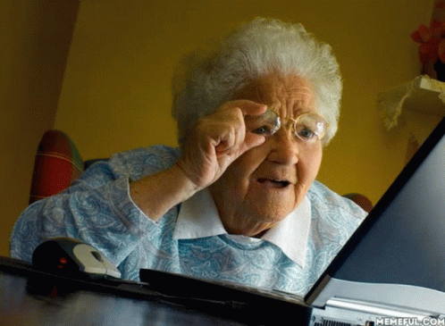 an elderly woman wearing glasses looks at a laptop computer