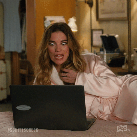 Schitt's Creek gif. Annie Murphy as Alexis lounges in a robe on a bed in front of an open laptop. She looks at the laptop, her eyes widening comically, twists her hair in her hand and says what appears as text, "Yum!"