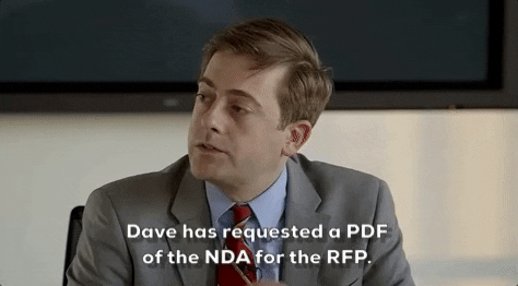 A white man in a blue shirt wearing a red striped tie and wearing a grey suit jacket. He is saying Dave has requested a PDF of the NDA for the RFP.