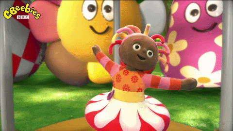 GIF of Upsy Daisy, a doll with brown skin, pink and yellow dreadlocked hair and a red flower skirt dancing in front of giant smiley faced flowers