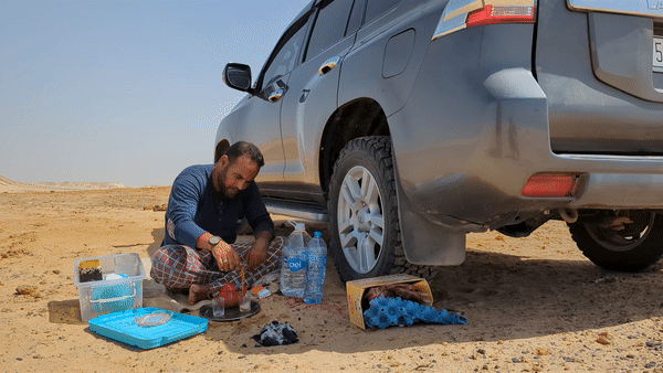 man sitting in shade of SUV pours Moroccan tea in the desert