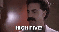 Movie gif. Sacha Baron Cohen as Borat gives a man an excited high five with a stiff hand.