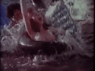 a man and a woman are swimming in a pool while a shark is swimming in the water .