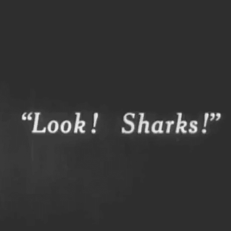 Gif from 1913 film 20000 Leagues Under the Sea showing an intercard that reads 'Look! Sharks!' and blurry underwater of sharks