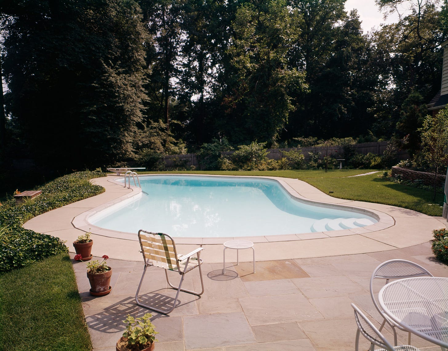 A midcentury kidneyshaped pool with a lawn chair next to it.