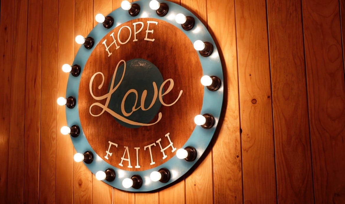 A sign saying hope, love, faith surrounded by a ring of lightbulbs.