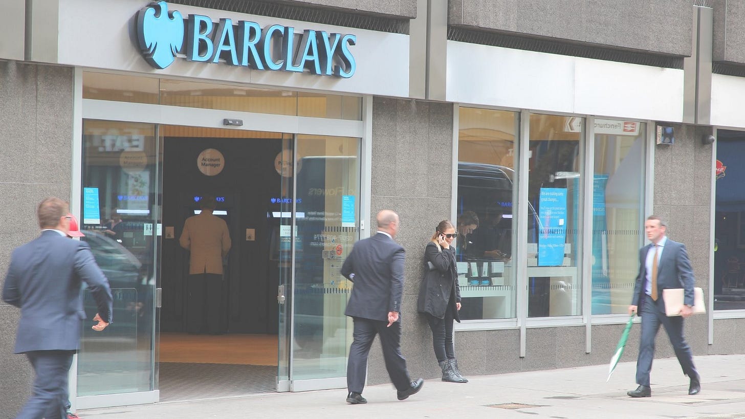 multiple people passing through a sidewalk in front of a Barclays bank