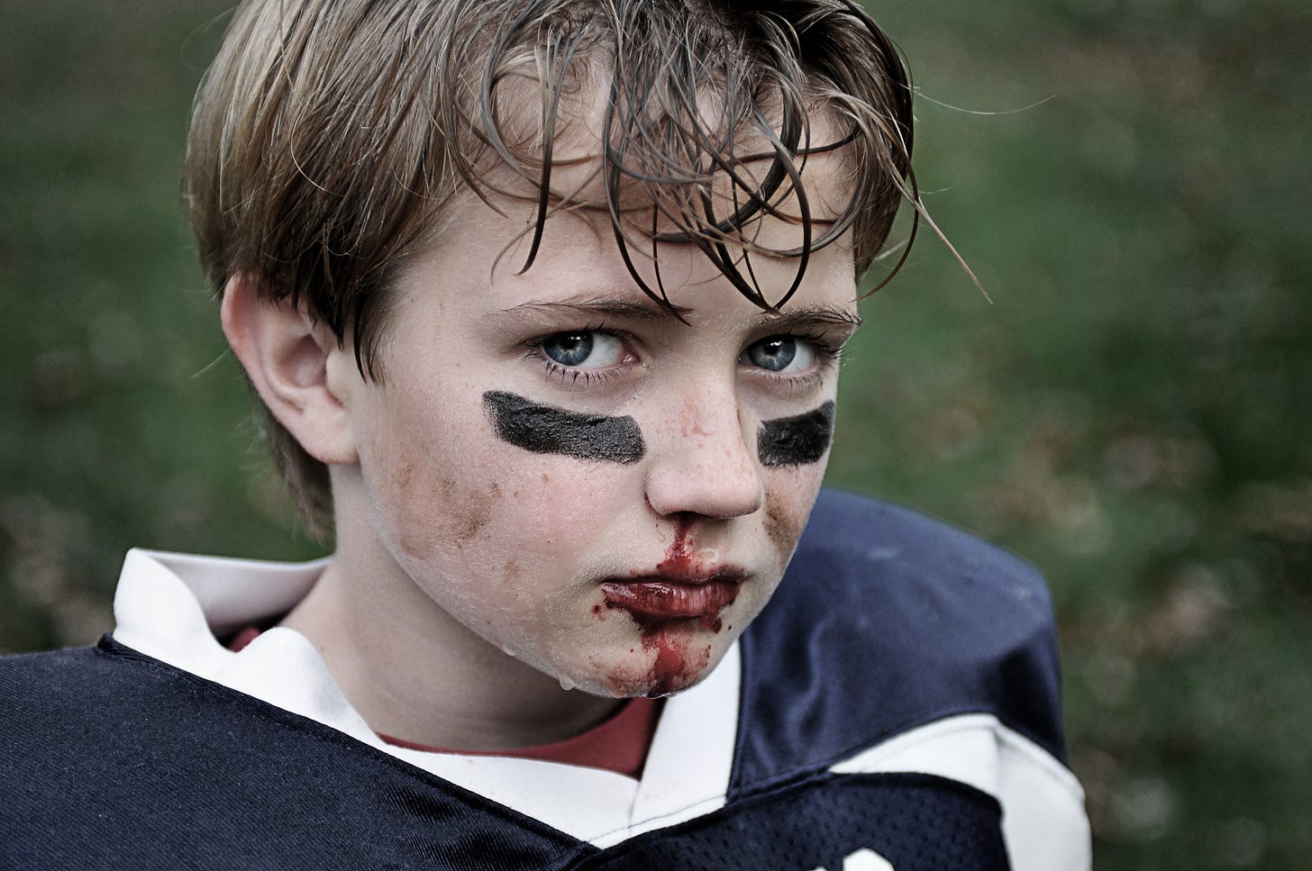 Young football player in pads with eye black and a bloody mouth
