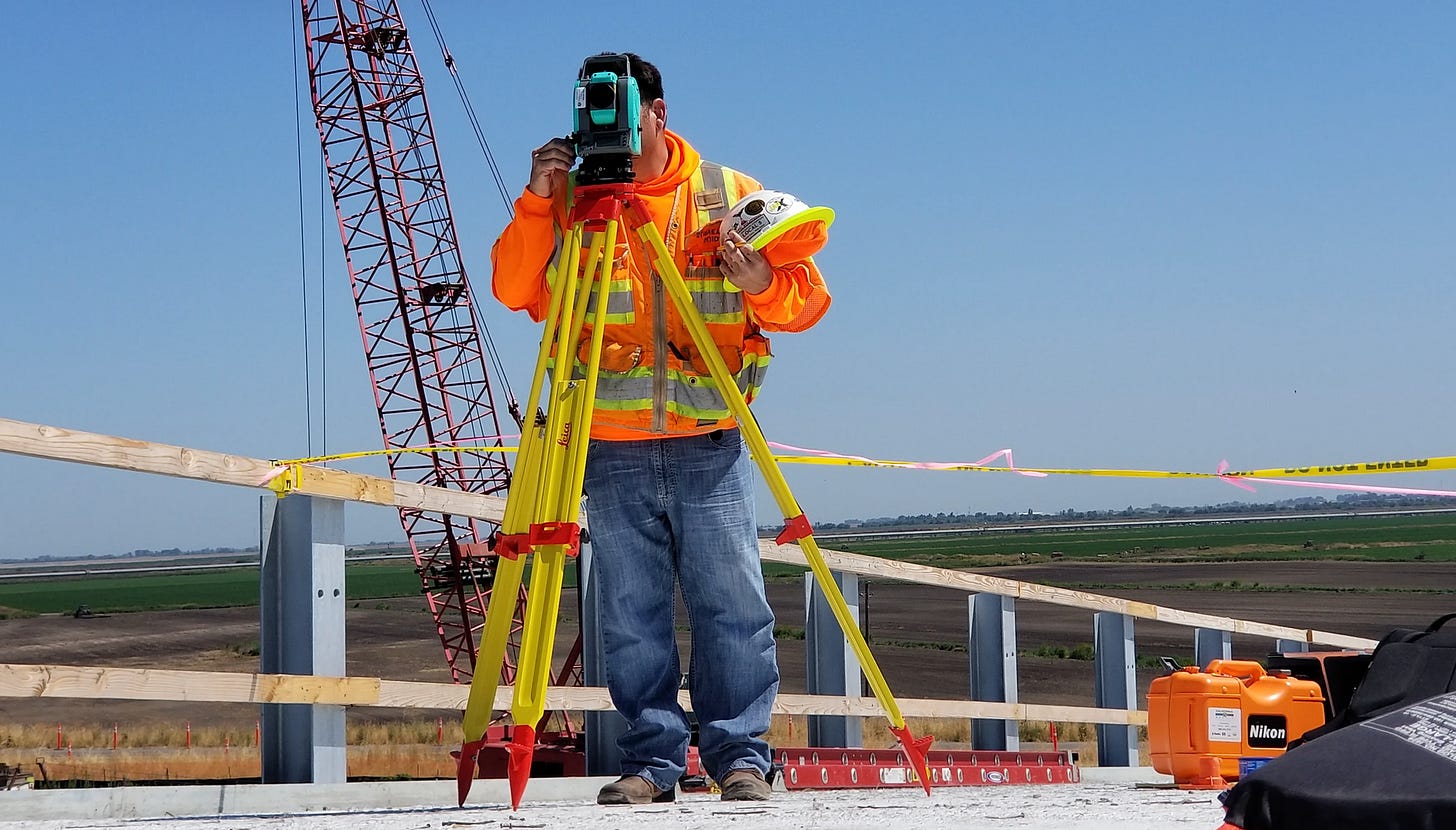 A man in high-vis vest using surveying equipment outdoors.