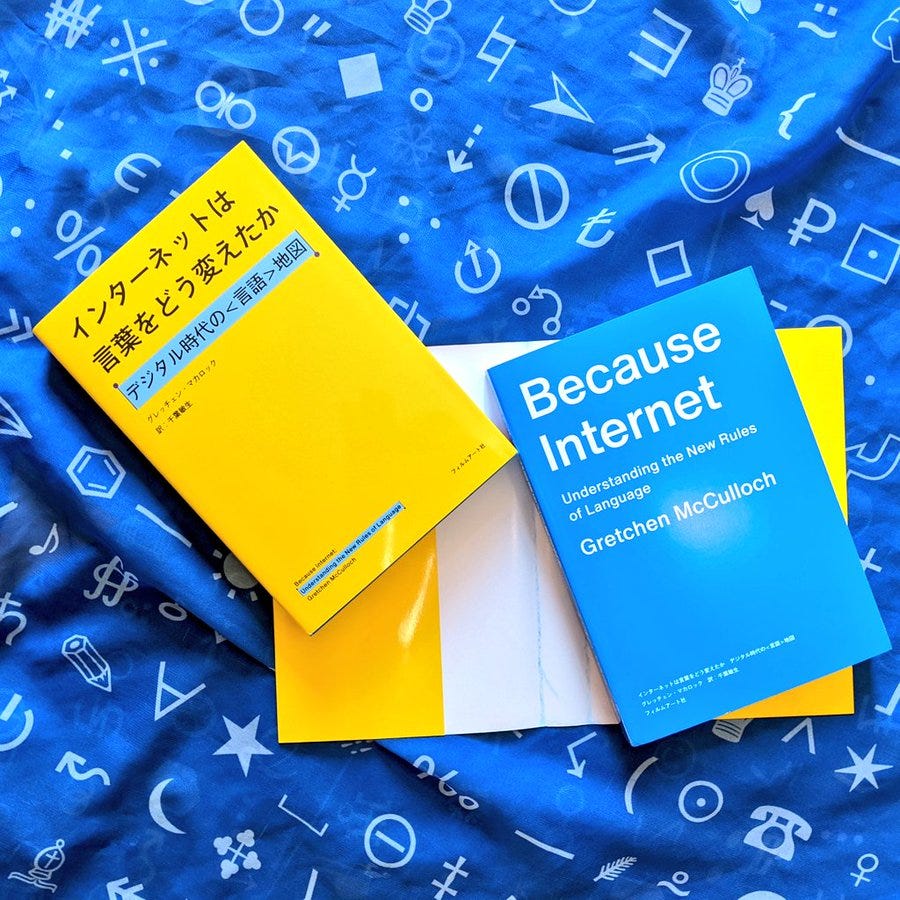 Image of Japanese editions of BECAUSE INTERNET on top of blue fabroc covered in symbols. One copy is in its yellow dust jacket; one shows the blue cover inside the jacket.