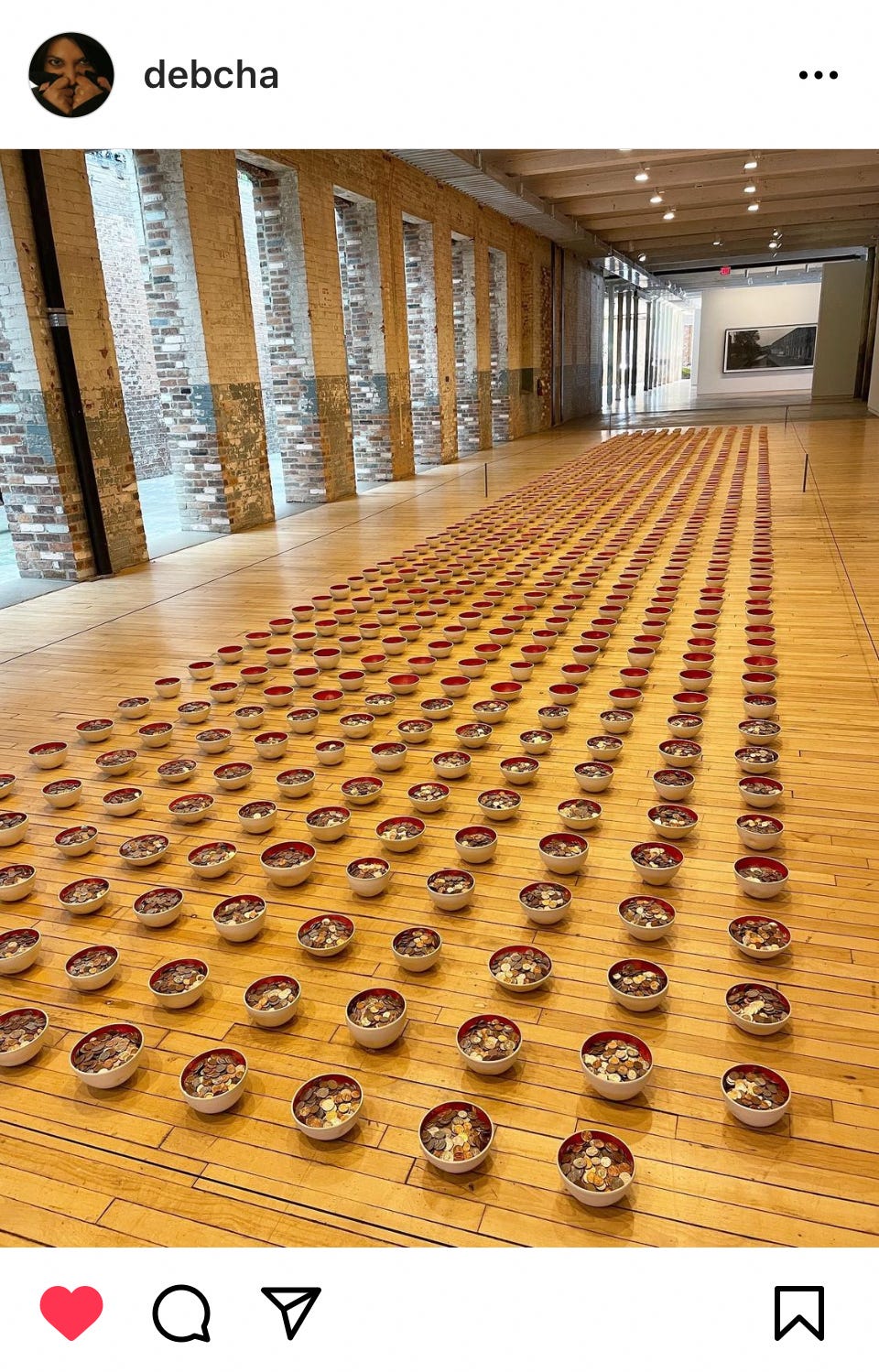 A grid of brass bowls lined up on a wooden floor, some filled with change.