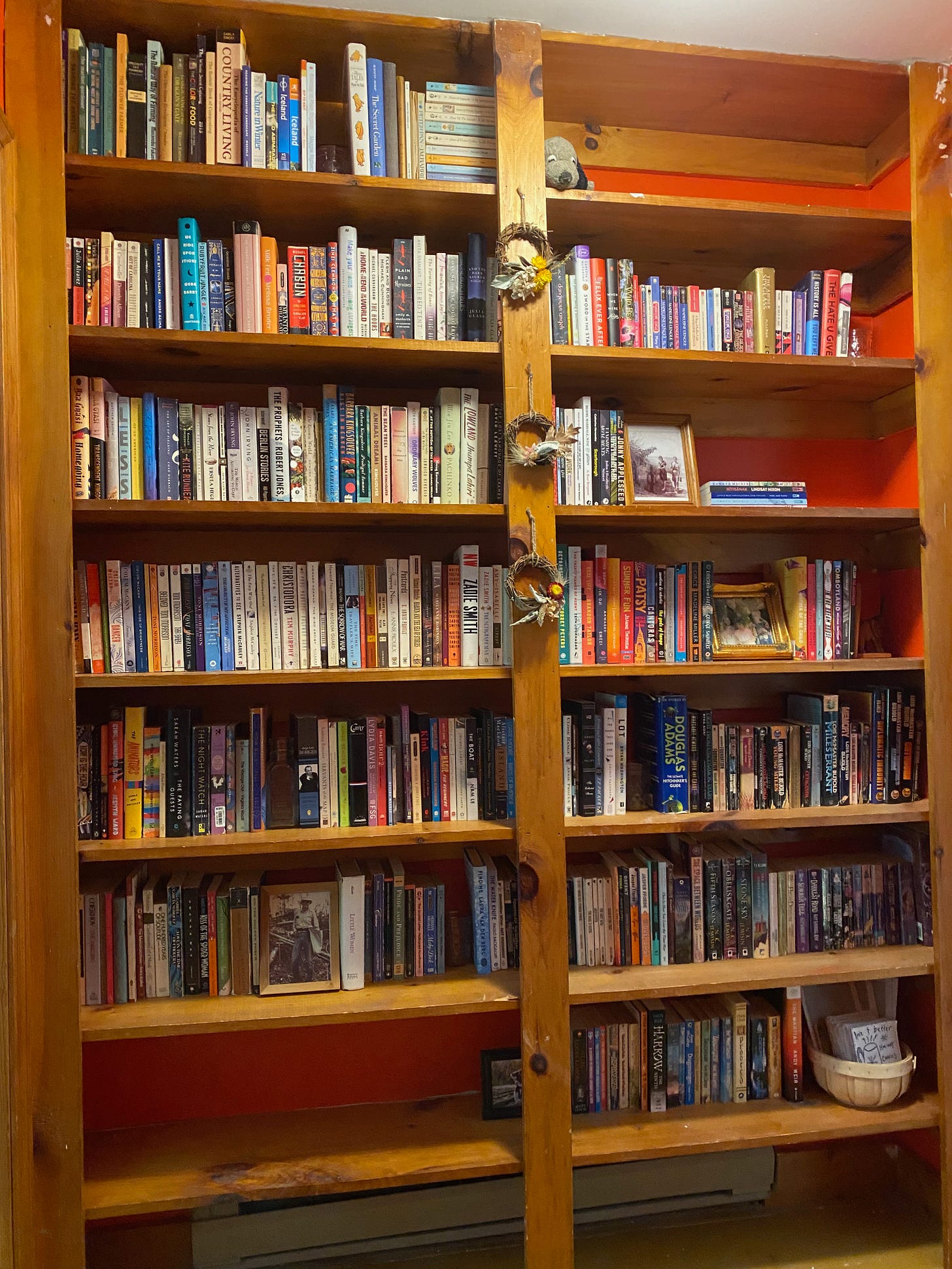 Two tall built in bookcases filled with books. A few of the top and bottom shelves are empty. Small dried flower wreathes hang on the wooden divider between the two shelves. Several photos are scattered among the books.