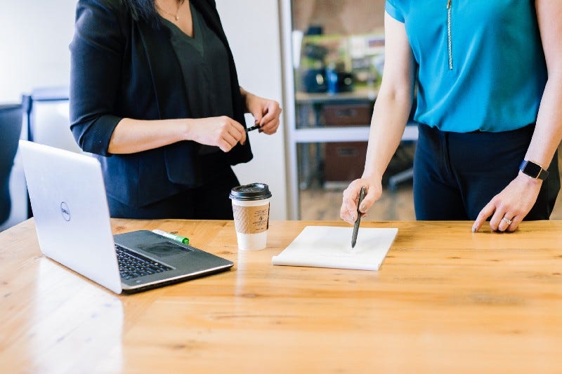 Two women talking standing and holding a pen