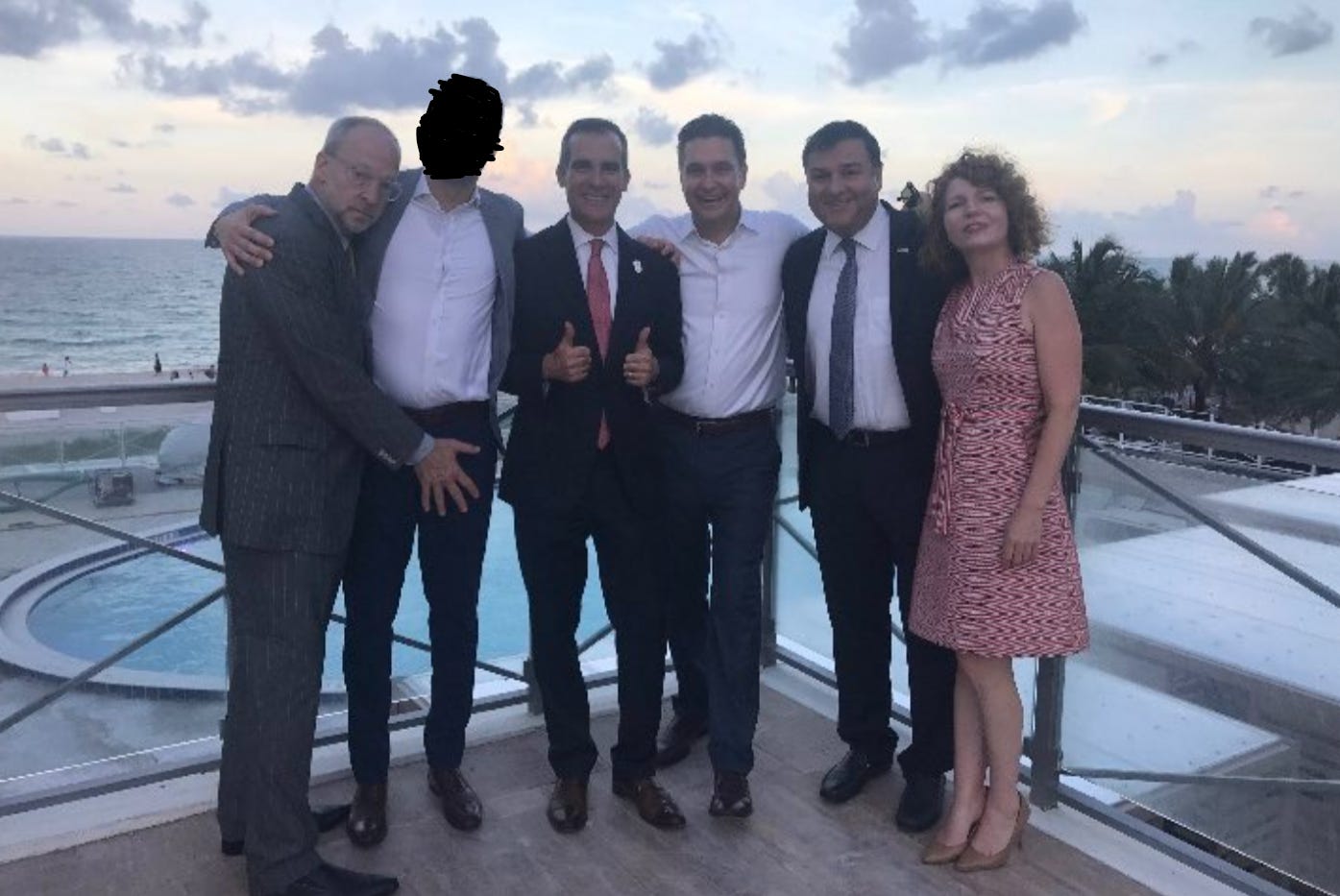 A photo of former Garcetti aide Rick Jacobs making an inappropriate gesture, with Mayor Garcetti giving a thumbs up. There are 6 people in the photo, and an island resort background.
