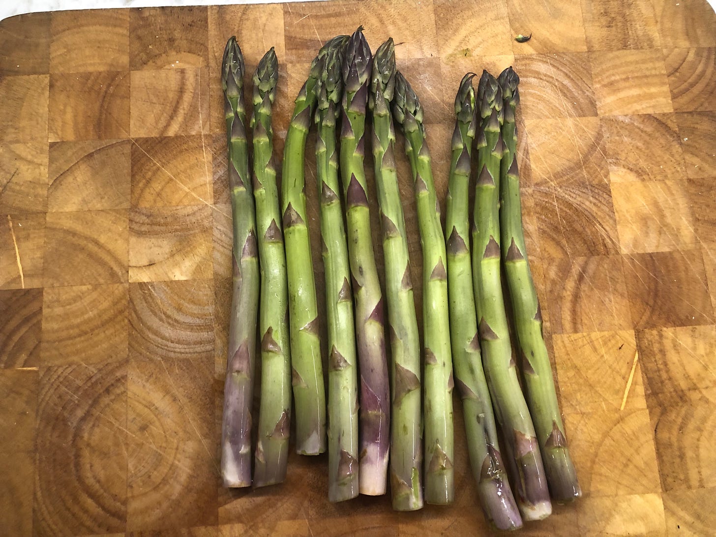 Ten spears of asparagus lying on a cutting board