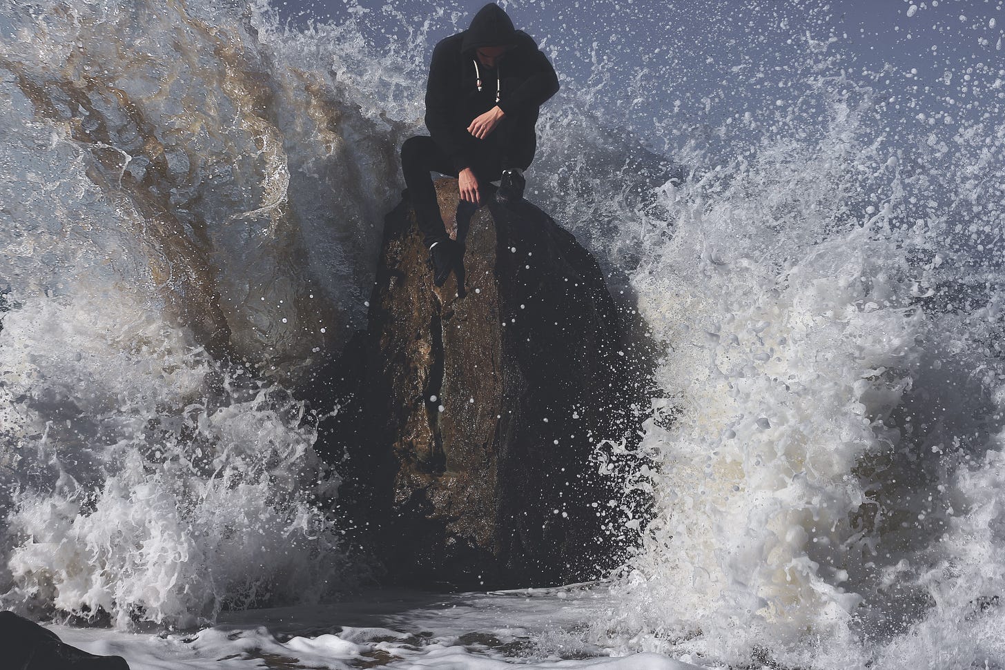 man seating on stone in between waving sea photo