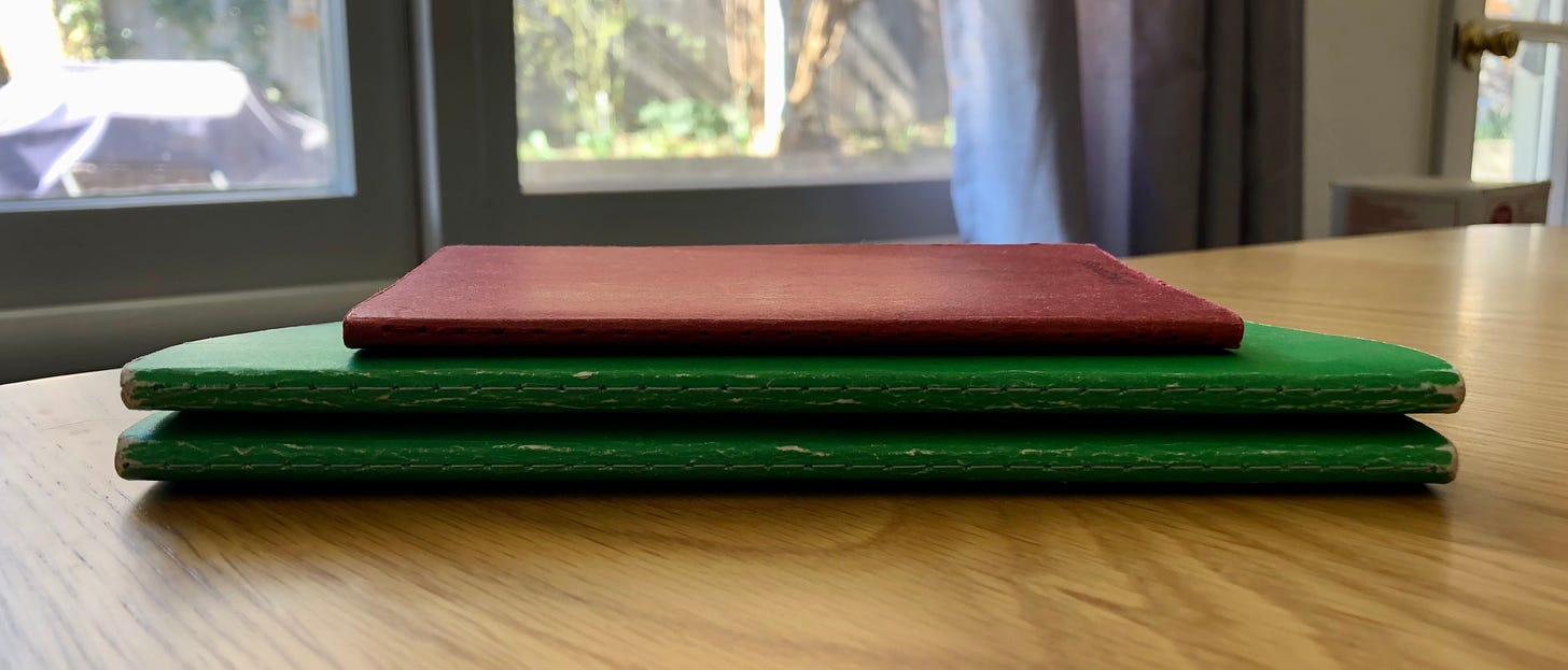a neat stack of three worn notebooks on a wood table with sunny windows behind