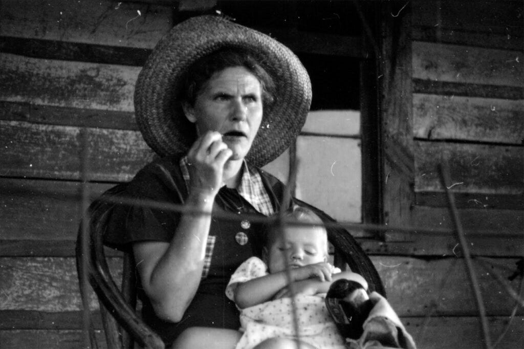 Myrtle Lawrence sits on her porch holding a sleeping baby | Flickr