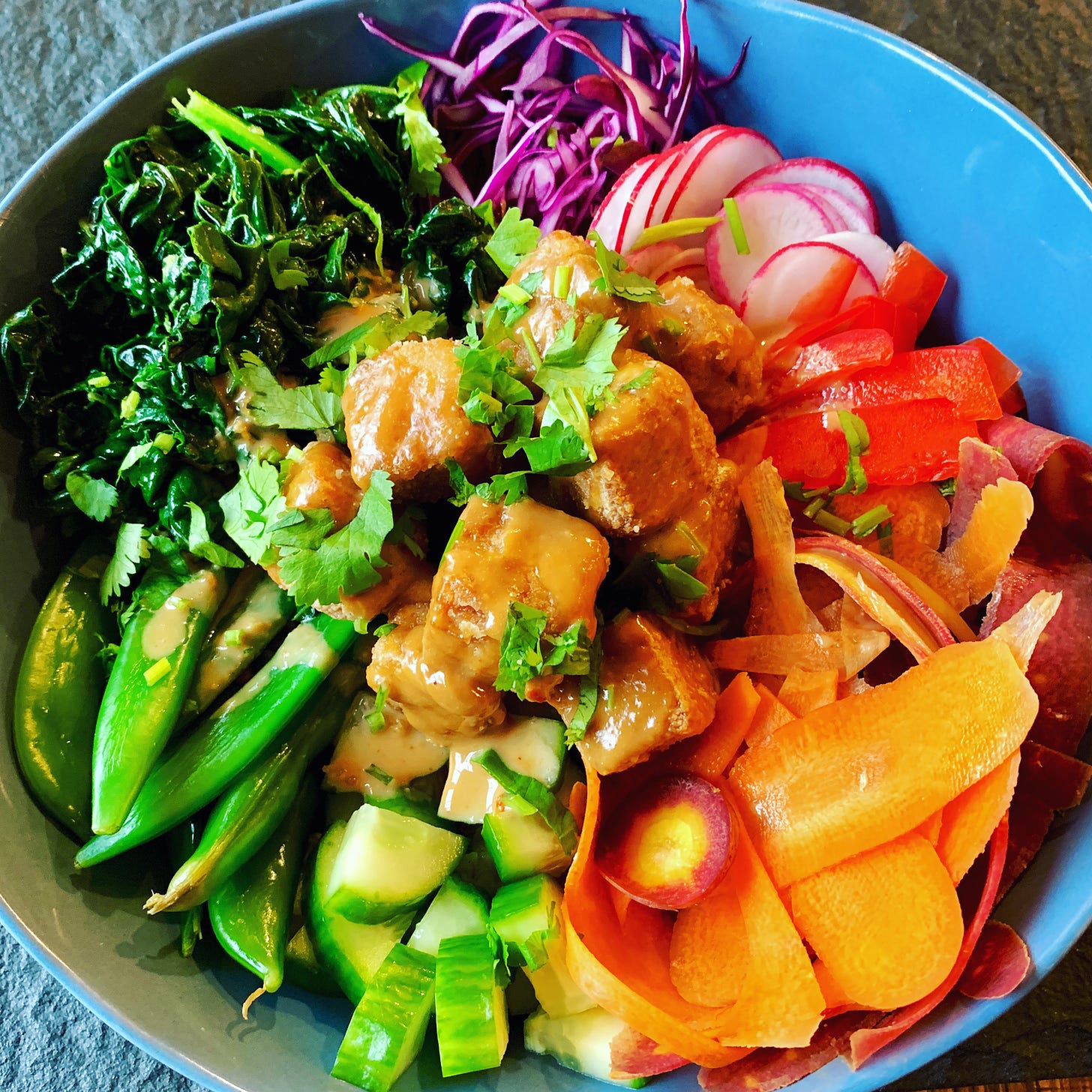 rainbow bowl filled with radish, red pepper, carrot (that I tried to cut fancy but was unruly and terrible), cucumbers, blanched sugar snap peas, blanched kale (tossed with the peanut sauce plus a little rice vinegar and extra salt), cabbage, crispy tofu, cilantro (not pictured: brown rice under all that.
