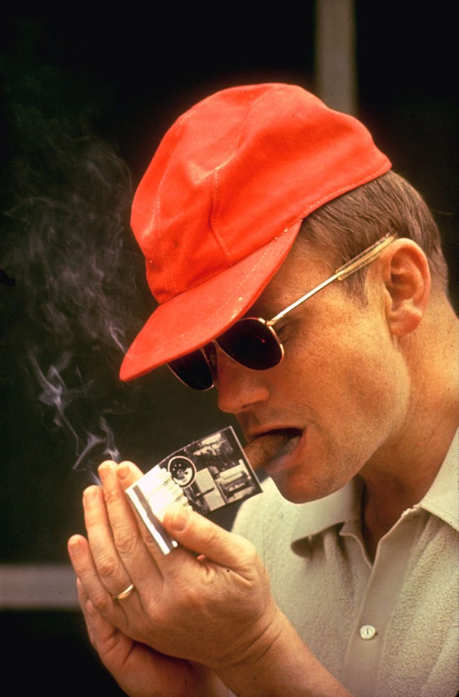 Armstrong in a red hat lighting a cigar.