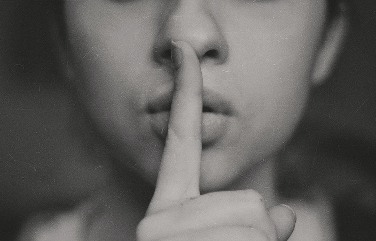 Black and white photo of a woman making the shush gesture. (Kristina Flour / Unsplash)