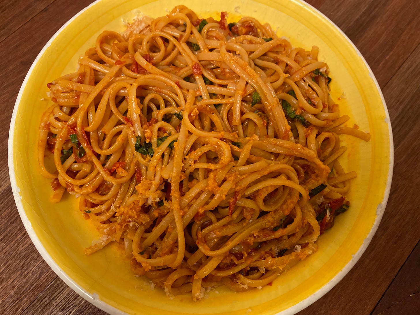 A shallow yellow bowl of linguine with tomato sauce.