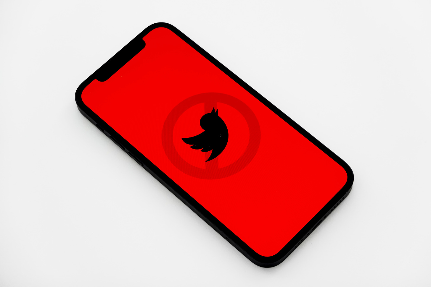 Photo of a black Twitter logo against a crimson red backdrop on a smartphone. (Jeremy Bezanger / Unsplash)