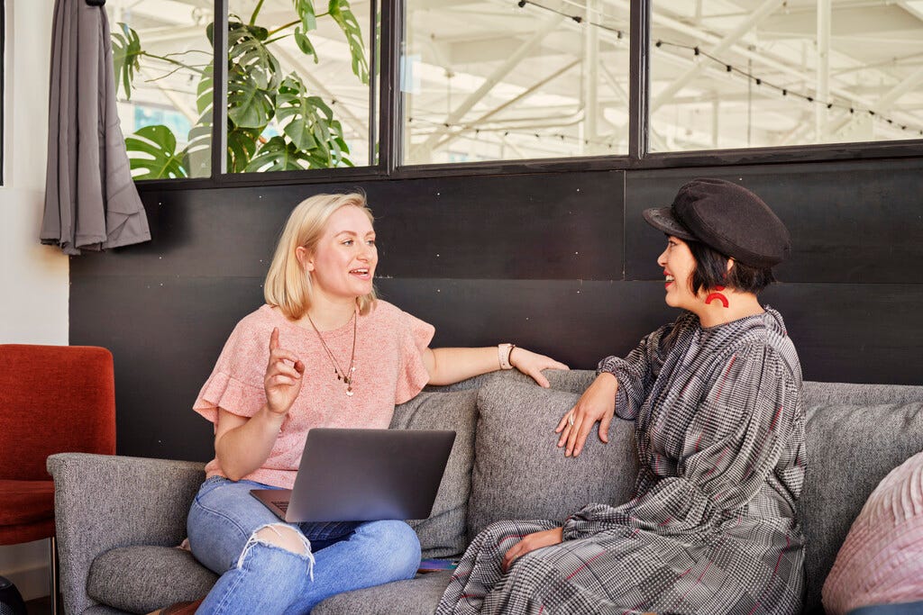 Photo of two people smiling and talking on a couch in an office