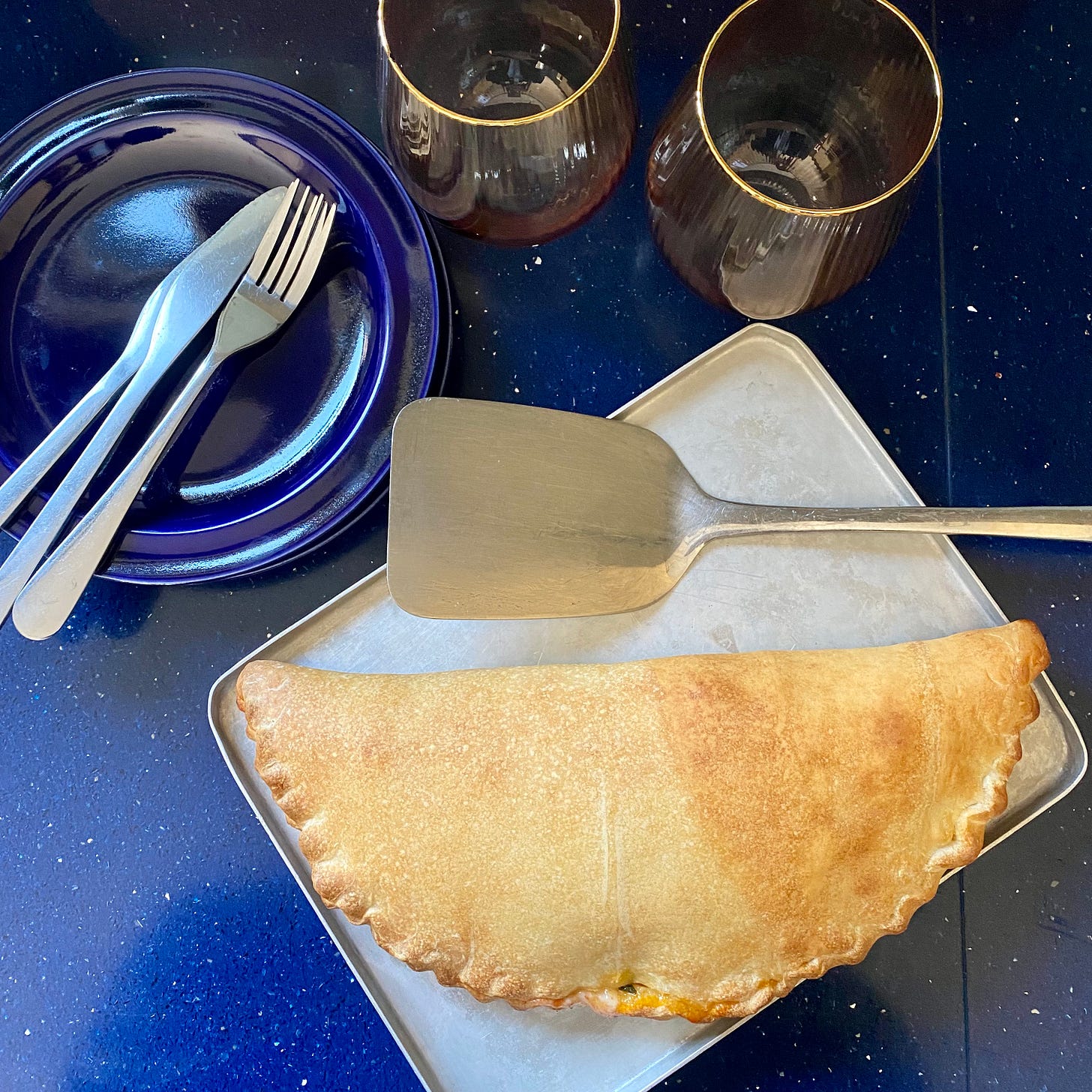 Calzone on a silver baking tray, blue plates with cutlery to the side. 