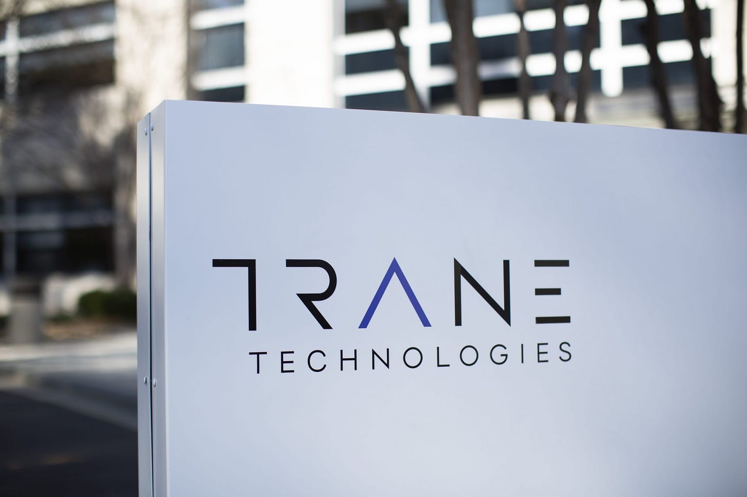Placa da Trane Technologies em destaque com prédio da empresa com desfoque atrás.