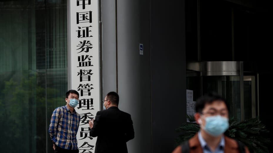 People wear protective masks as they stand outside of the China Securities Regulatory Commission (CSRC) in the Financial Street on April 17, 2020 in Beijing,