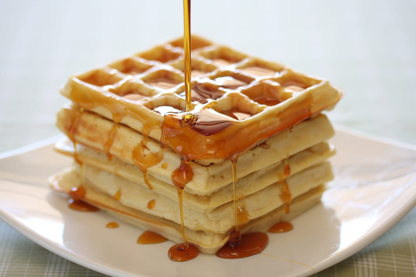 A stack of waffles with syrup pouring from above.