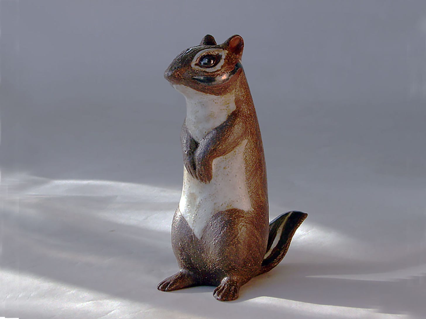 The classic Andersen Design Standing Chipmunk. The back and face is decorated in brown slip with glossy ebony eyes surrounded by a rim of matte white. The belly is also matte white and the tail is glossy ebony with brown and white stripes.