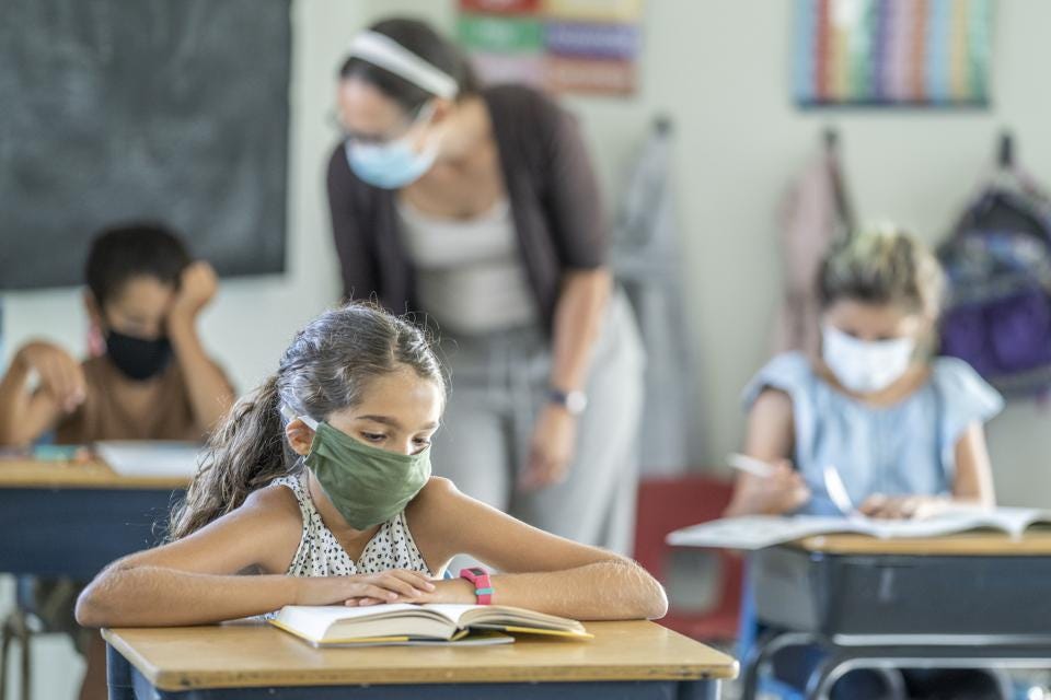 Female students wearing a green face mask reading a book at a desk. 