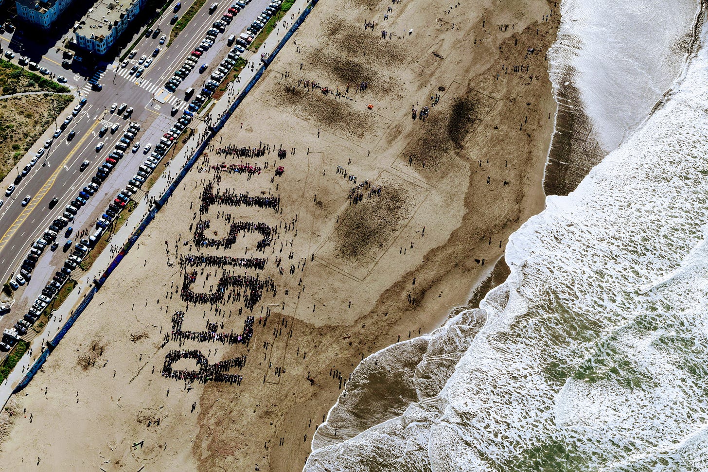 A beach with people standing in specific locations to spell out the word Resist