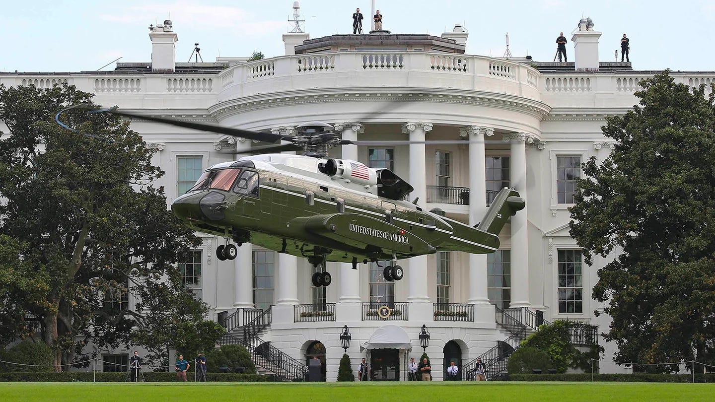 A green helicopter landing on the lawn in front of the White House