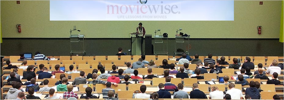 A large lecture hall filled with students watching a speaker on stage with the word ‘moviewise’ displayed on a banner.