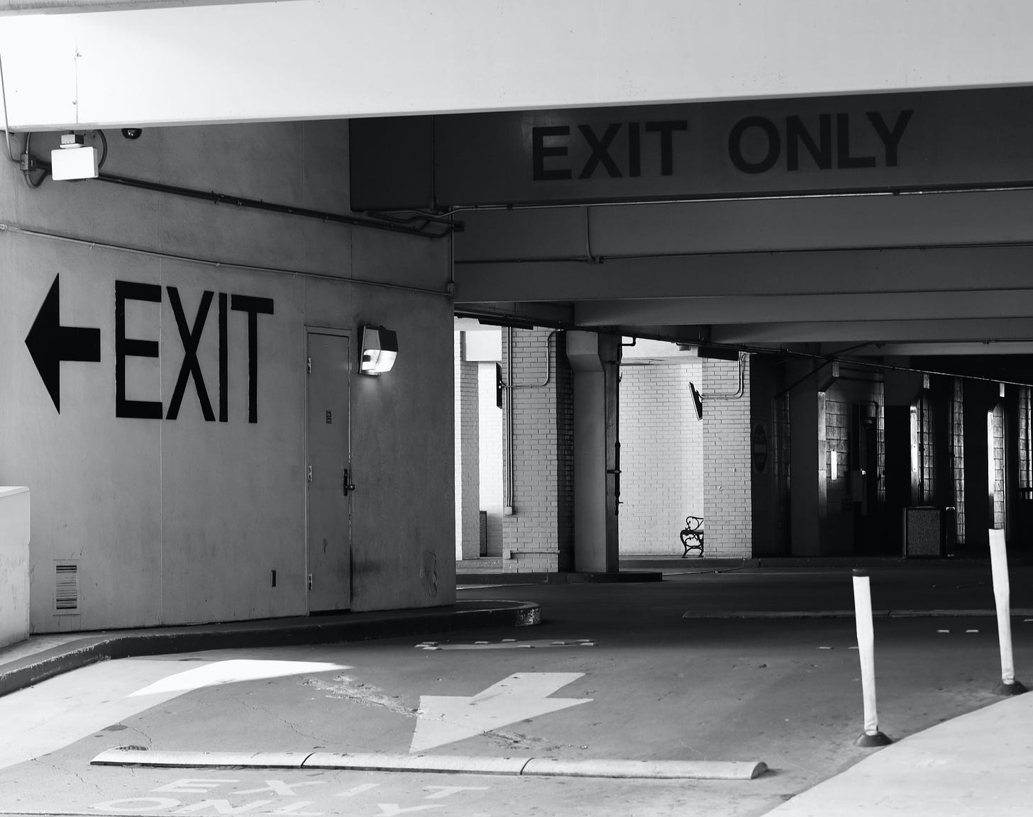 A grayscale photo of a car park, showing exit signs prominently.