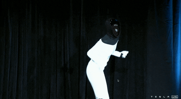 Una persona vestita da umanoide, in tuta bianca, balla su un palco.