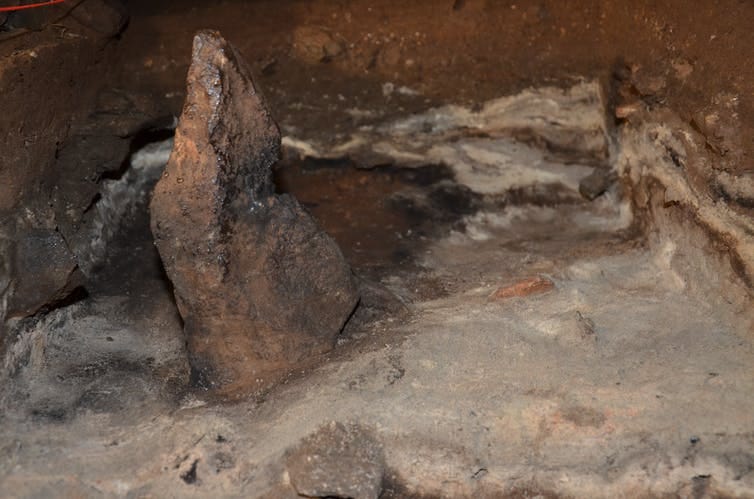 A small elongated stone standing upright in ashy sediments.