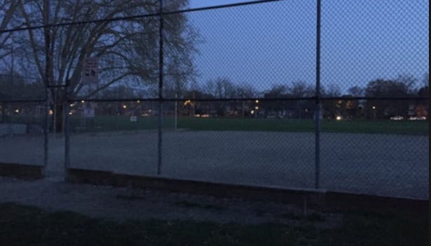 a softball diamond through a fence in the evening