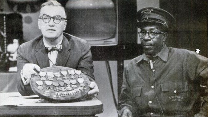 White man holding board covered in military medals with black man in elevator operator uniform