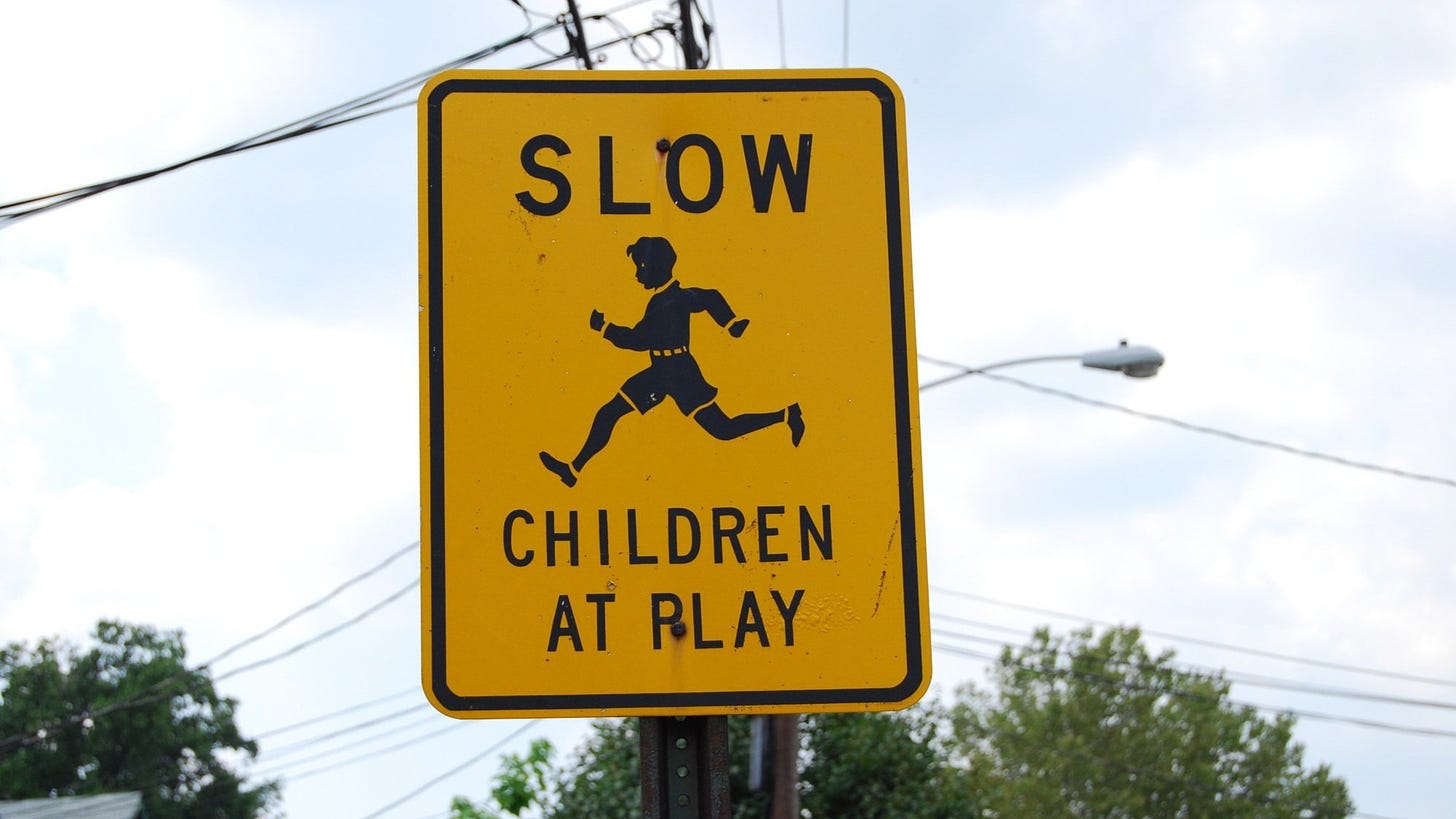A yellow street sign featuring a picture of a running child and the words "Slow. Children at play."