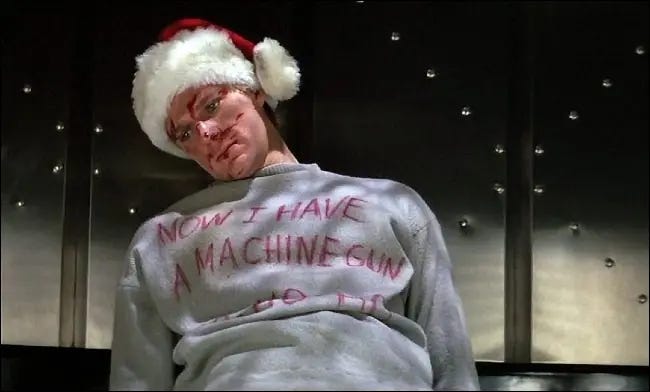 A bad guy from the film wearing a Santa hat and blood across his face. His gray sweater says "Now I have a machine gun ho ho ho".