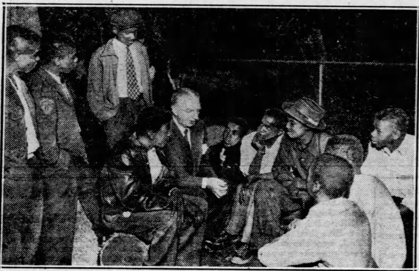 Image shows an older white man speaking with several Black teenage boys who are gathered around him listening.