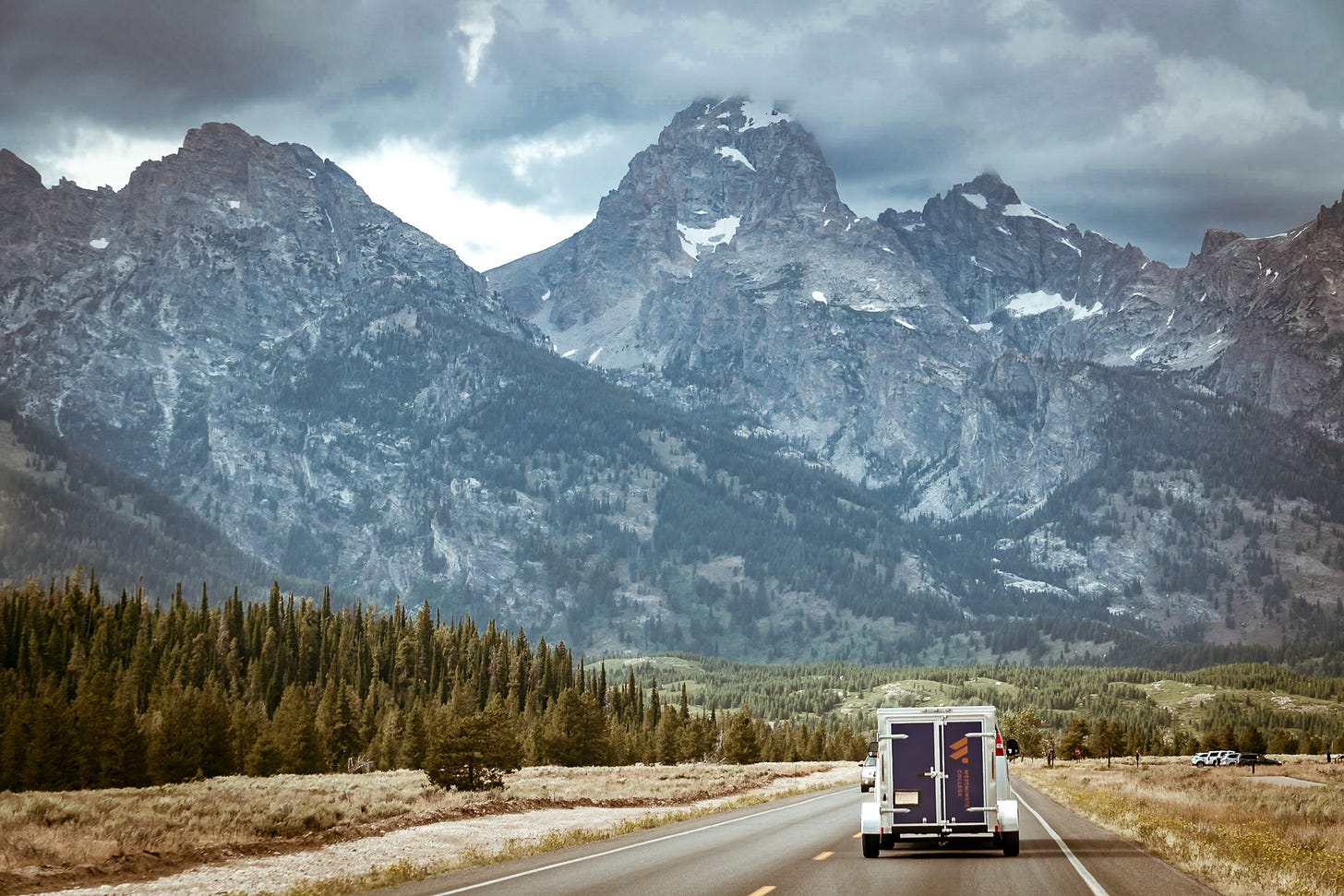a van travels on a road with the Grand Tetons in the background